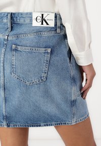Τζιν μίνι φούστα σε ανοιχτό μπλε, με πίσω τσέπη και λευκή ετικέτα με το λογότυπο "Calvin Klein Jeans" στη μέση.