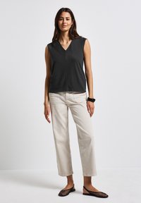 Top senza maniche di un grigio scuro con scollo a V e orlo dritto, abbinato a pantaloni a gamba larga di un beige chiaro e scarpe nere in rete. Design semplice e pulito.