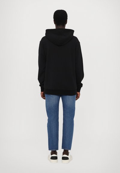 Sweat-shirt noir à capuche avec une coupe décontractée, des poignets et un ourlet côtelés, associé à un jean bleu à jambes droites et des baskets noir et blanc.