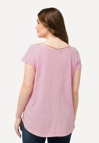 Top rosa a maniche corte con scollo rotondo, caratterizzato da dettagli di taglio sulla schiena e un orlo curvo. Tessuto morbido e leggero.