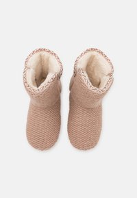 Knitted plush slippers in light beige, with a soft faux fur lining and decorative patterned trim around the ankle.