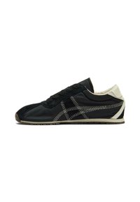 Zapatilla negra y beige, hecha de una mezcla de tejido suave y ante. Presenta costuras contrastantes, puntera redondeada y suela texturizada.