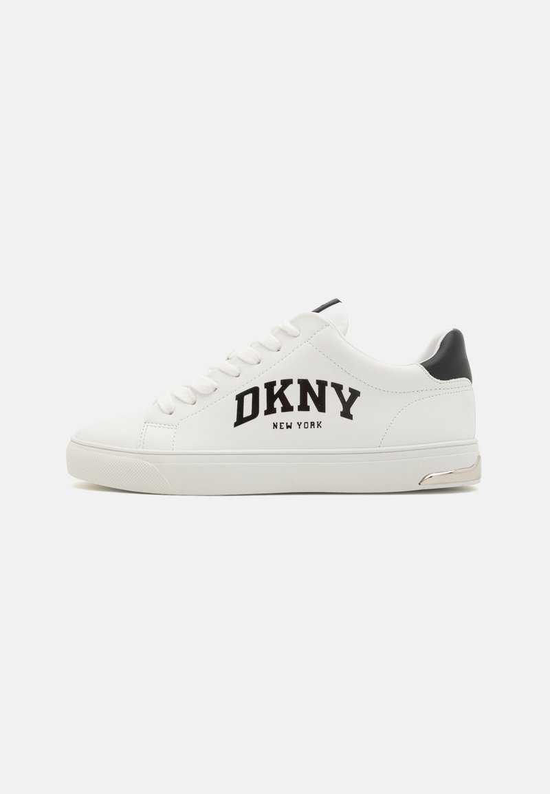 Hvite lær sneakers med svarte detaljer, med "DKNY NEW YORK" logo, snøring, og en sølvfarget detalj på hælen.
