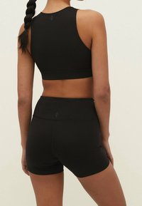 Zwarte sportieve crop top en hoogdrogende shorts gemaakt van rekbaar materiaal. De top heeft een racerback ontwerp en subtiele logo-details.