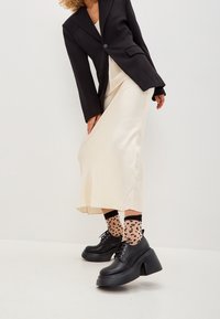 Black blazer, cream satin midi skirt, black platform shoes with thick soles, and leopard print socks. Smooth textures, tailored design.