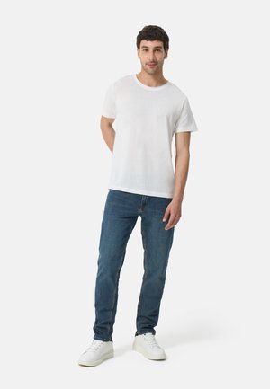 Hvid kortærmet t-shirt med rund halsudskæring, parret med blå denim jeans. Modellen bærer hvide sneakers. Enkel design, letvægtsmateriale.