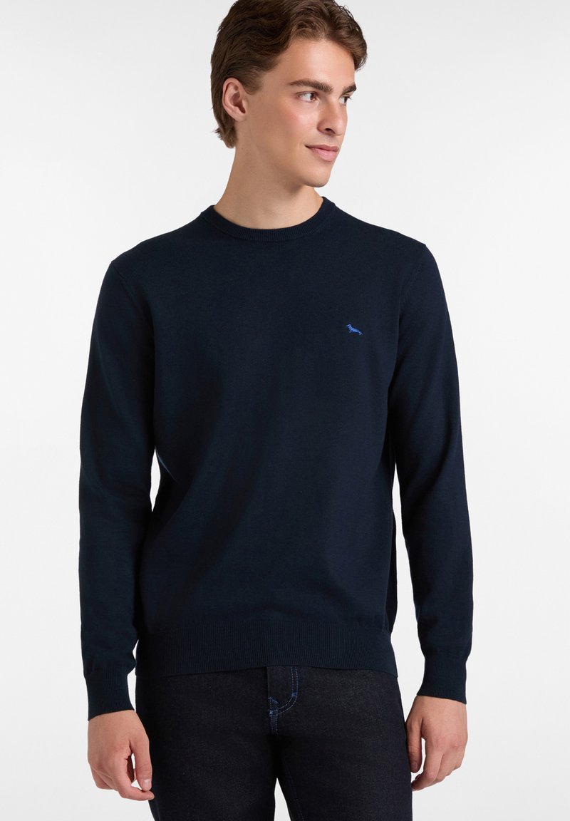 Jersey de punto azul marino con mangas largas, cuello redondo y puños acanalados. Presenta un pequeño logotipo azul en el pecho.