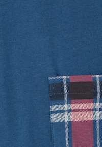 Tela de algodón azul con un bolsillo de cuadros texturizados en rojo, negro y blanco, con franjas horizontales y verticales.