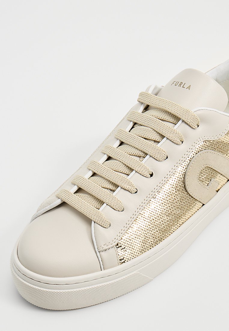 Zapatilla de cuero beige con panel lateral de lentejuelas doradas, cordones planos, punta redondeada y suela texturizada. Nombre de la marca "Furla" grabado en la lengüeta.
