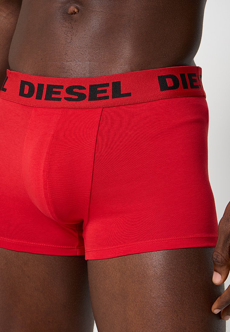 Torso maschile che indossa boxer rossi Diesel con fascetta nera con logo su uno sfondo neutro.