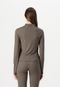 Langarm jumpsuit in een houndstooth patroon, met een zwart en beige kleurenschema en een getailleerde silhouet met een opstaande kraag.
