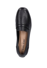 Zapato negro de cuero tipo slip-on con punta redondeada, correa decorativa en la parte superior y una suela intermedia texturizada.