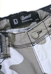 Tissu à motifs camouflage dans des tons de gris et de noir, avec un bouton en métal et une étiquette 'Brandit' ; détails de couture visibles au niveau de la taille.