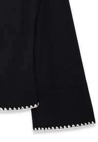 Black fabric featuring a wide sleeve with a scalloped, white fringe hem. Smooth texture and tailored shape, highlighting a minimalistic design.