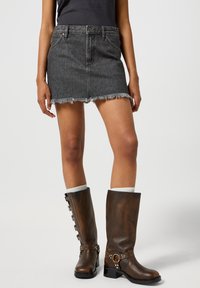 Tume denim mini seelik franatatud servaga, keha lähedane disain, koos põlveni ulatuvate pruunide nahast saapadega, millel on dekoratiivsed metallaktsendid.