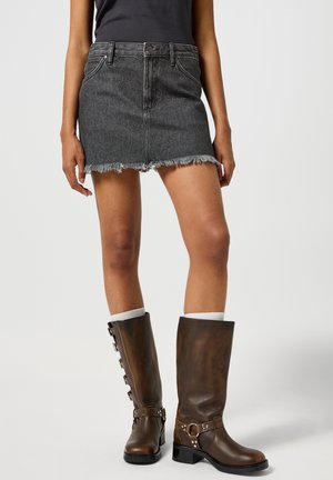 Tmavomodrá mini sukňa z denimu s frayed lemom, priliehavý strih, skombinovaná s hnedými koženými čižmami po kolená so dekoratívnymi kovovými akcentmi.