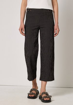 Sorte cropped bukser med striber, brugt med sorte sandaler med spænde og en hvid top, vist fra taljen til fødderne.