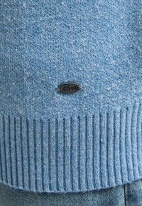 Lichtblauwe trui met een gestructureerd oppervlak en subtiele spikkels. Geribbelde onderrand en een klein metalen label met het "Petrol" logo onderaan.