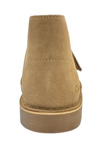 Vista posteriore di un stivaletto alla caviglia in suede marrone chiaro con cuciture visibili e tacco in legno impilato.