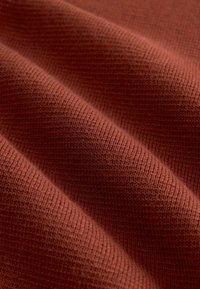 Texturovaná tkanina v bohaté cihlové barvě, s ribbovaným vzorem a viditelnými pletenými liniemi a měkkou, tkanou strukturou.