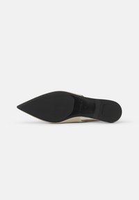 Zapato de tacón alto beige con punta afilada, parte superior de cuero liso y suela de goma negra. Presenta un diseño minimalista y sin hardware visible.