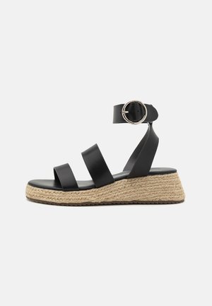 Zwarte leren wedge sandaal met drie gordelontwerpen, enkelgesp en natuurlijke jute-stijl touwdetails rond het plateau.
