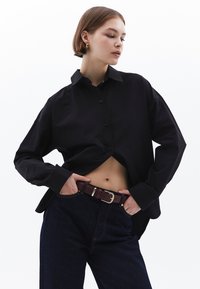 Zwarte oversized button-up shirt met een spread collar, voorzien van lange mouwen, gecombineerd met donkerdenim jeans en een bruine leren riem.
