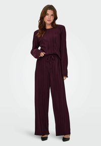 Ensemble deux pièces plissé bordeaux avec des manches longues, un haut ample, un pantalon à taille élastique et une texture douce. Chaussures noires.