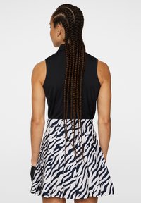 Svart ärmlös topp i kombination med en vit kjol med ett marinblått zebramönster. Kjolen har veck och fickor. Håret är i långa flätor.