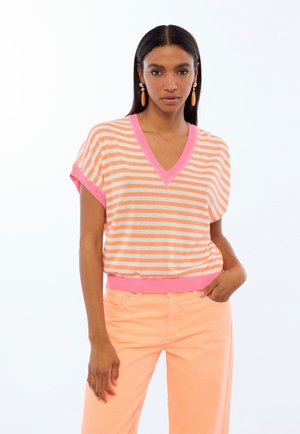Top de manga corta a rayas en naranja y rosa con escote en V y puños acanalados; combinado con pantalones de pierna ancha de color durazno.