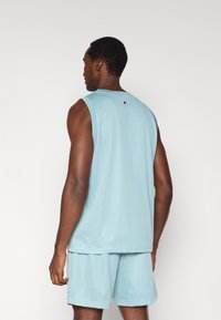 Ανοιχτό μπλε αμάνικη μπλουζά με δίχτυ και σορτς, με στρογγυλή λαιμόκοψη και χωρίς μανίκια. Μικρό λογότυπο στο πίσω μέρος. Απαλή υφή και αναπνεύσιμο υλικό.