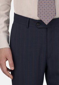 Tumed pinnatud püksid siledast materjalist, millel on nööbiväär ja küljetasku, koos triibulise särgiga ja mustrilise lipsuga.