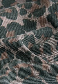 Cotton fabric with a camouflage pattern in dark green and beige, featuring a textured weave and visible stitching along edges.