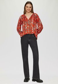 Rode en zwarte slangenprint blouse met een V-hals, lange mouwen en een relaxed fit; gecombineerd met donkere flared jeans en zwarte enkellaarsjes.