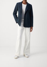 Námornícky blejzr s jedním knoflíkem, klopovými límci a dvěma předními kapsami, v kombinaci s bílými širokými kalhotami a bílými teniskami.