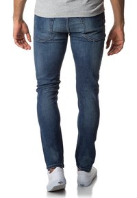 Slim-fit modré džíny s zadními kapsami, viditelným šitím a hladkým povrchem. Nosit s bílými teniskami.