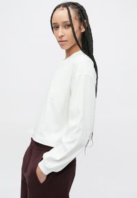 Hvid, kort sweatshirt med lange ærmer og rund halsudskæring, kombineret med bordeaux bukser med afslappet pasform og blød tekstur.