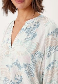 Blouse légère imprimée aux couleurs pastel, avec un col en V, une texture subtile et des motifs abstraits en forme de vagues bleues, roses et beiges.