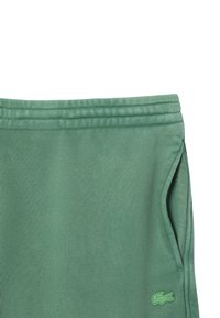 Pantalons de survêtement en coton verts avec taille élastique, poches latérales et un petit logo brodé. Texture lisse et design décontracté.