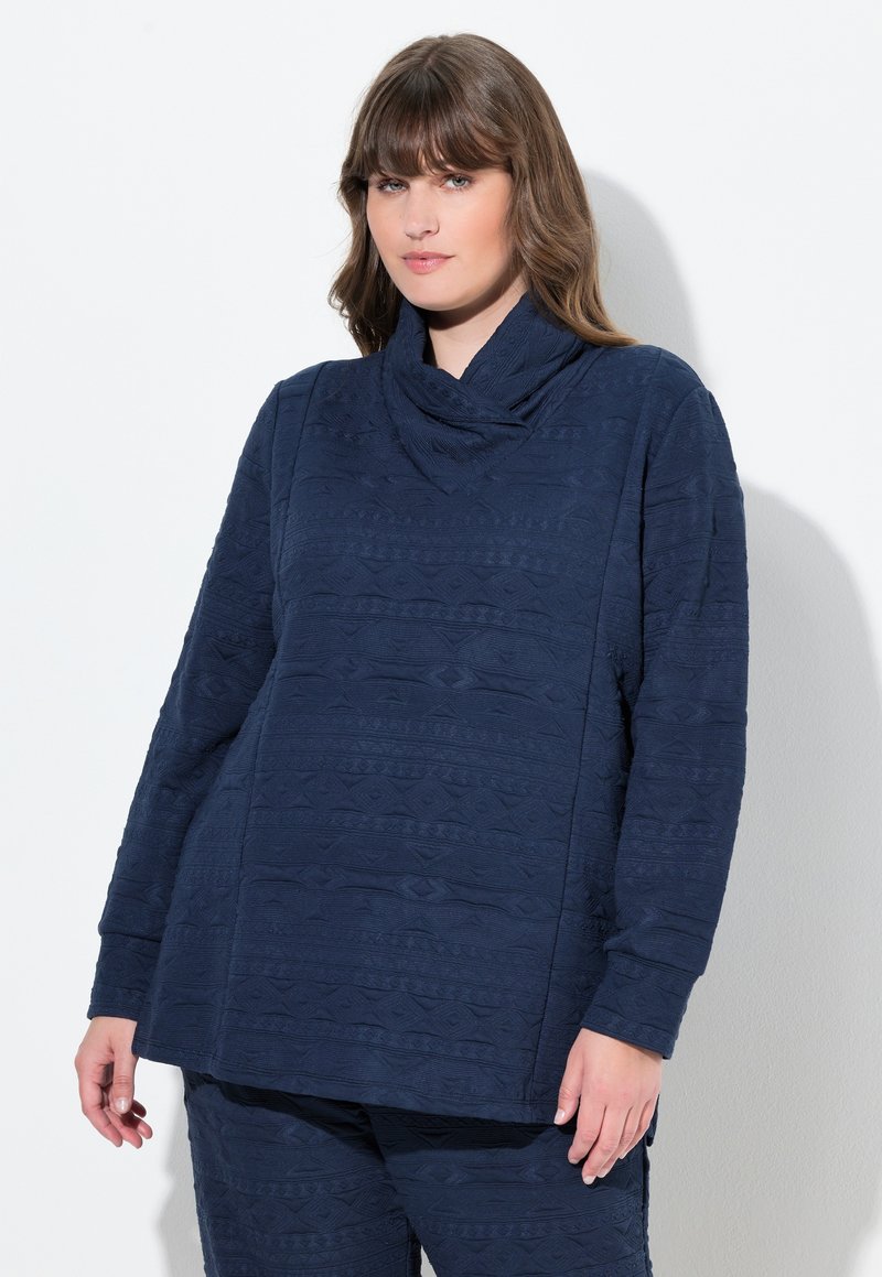 Maglietta a maniche lunghe blu navy con collo a cowl, tessuto strutturato con un motivo geometrico e vestibilità rilassata. Abbinata a pantaloni coordinati.