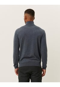 Grijze gebreide trui met een hoge kraag, met een gestructureerde afwerking en geribbelde manchetten. De stof lijkt zacht en licht van gewicht.