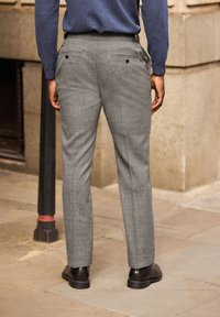 Pantaloni grigi a motivo con una vestibilità sartoriale, caratterizzati da una vita piatta, due tasche posteriori con bottone, indossati con scarpe nere.