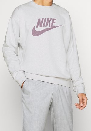 Sweatshirt gris clair avec un logo Nike violet. Présente un col ras du cou et des poignets côtelés, fabriqué en tissu doux et texturé.