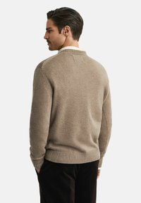 Béžový pletený svetr s ribovaným lemem a límcem, s texturovaným povrchem a jemnými švy, zobrazený ze zadní strany.