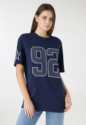 Granatowy bawełniany t-shirt z dużym białym numerem „92” wykonanym z kropek na przodzie oraz gwiazdą na lewym rękawie. Standardowy fason.