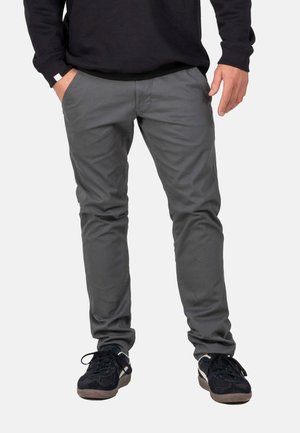 Graue, schlank geschnittene Hose aus leichtem Stoff mit glatter Textur und seitlichen Taschen. Kombiniert mit schwarzen Sportschuhen.