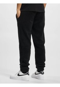 Svart, lodden fleece joggebukser med side lommer, elastiske mansjetter og avslappet passform, kombinert med hvite sneakers med svarte detaljer.