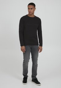 Chemise noire à manches longues avec un panneau supérieur texturé, assortie à un jean gris slim-fit et des baskets noires, sur fond neutre.
