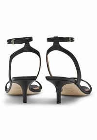Black leather high-heeled sandals with ankle straps, open-toe design, slim heels, and a smooth texture. Interior features branding.