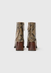 Bottines avec un motif en cuir de serpent, une palette de couleurs beige et marron, des zips latéraux et des talons en bois carrés.